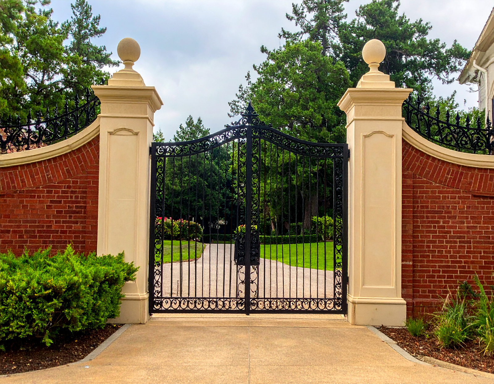 A grand estate entrance with red brick walls curving inward topped with ornate black 723964 - San Antonio Deck and Fence Works Black wrought iron gate, brick pillars.-deck builder-San Antonio, Texas