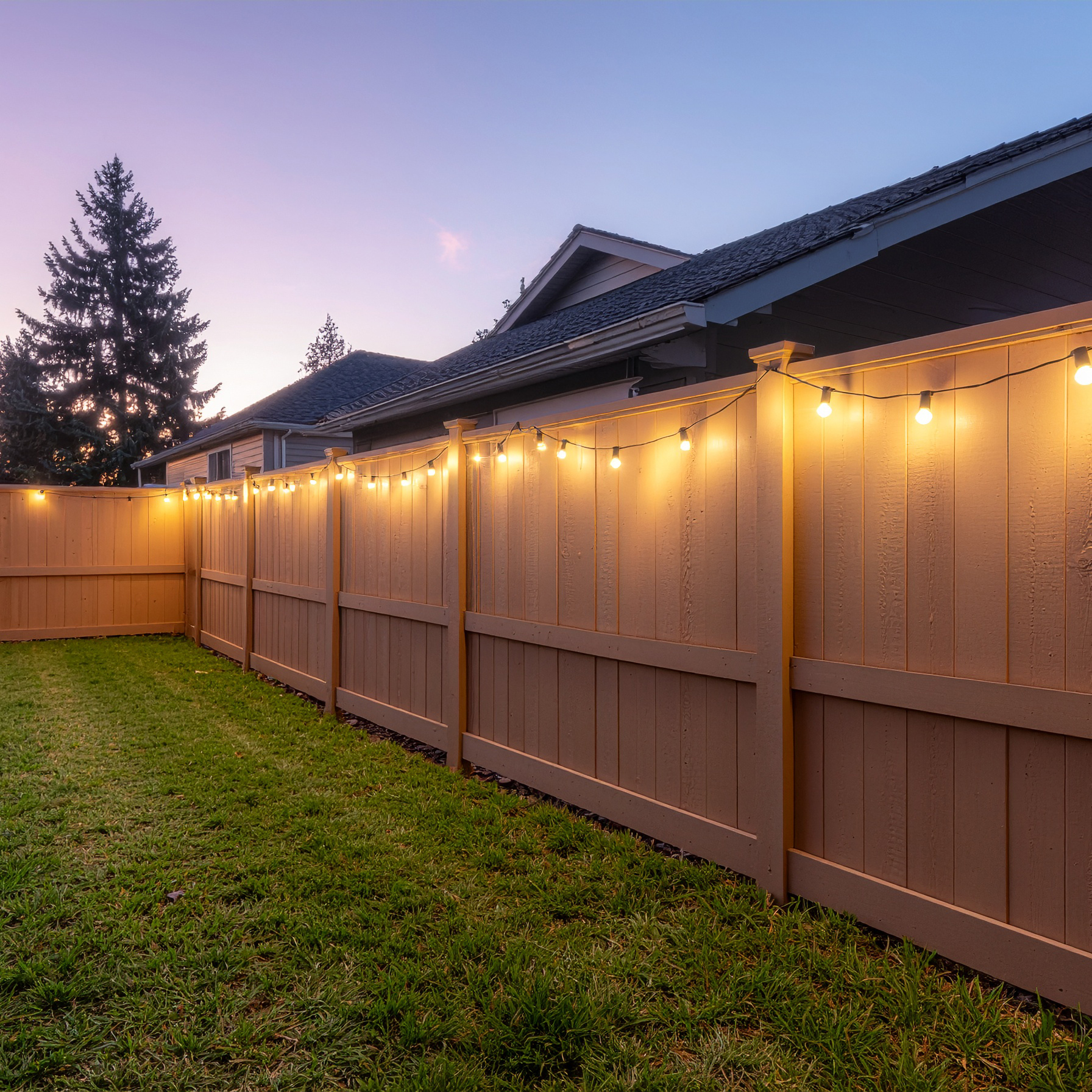 A private backyard enclosed by a cedar wooden privacy fence made of vertical planks w 158192 - San Antonio Deck and Fence Works Brown wooden fence with string lights.-deck builder-San Antonio, Texas
