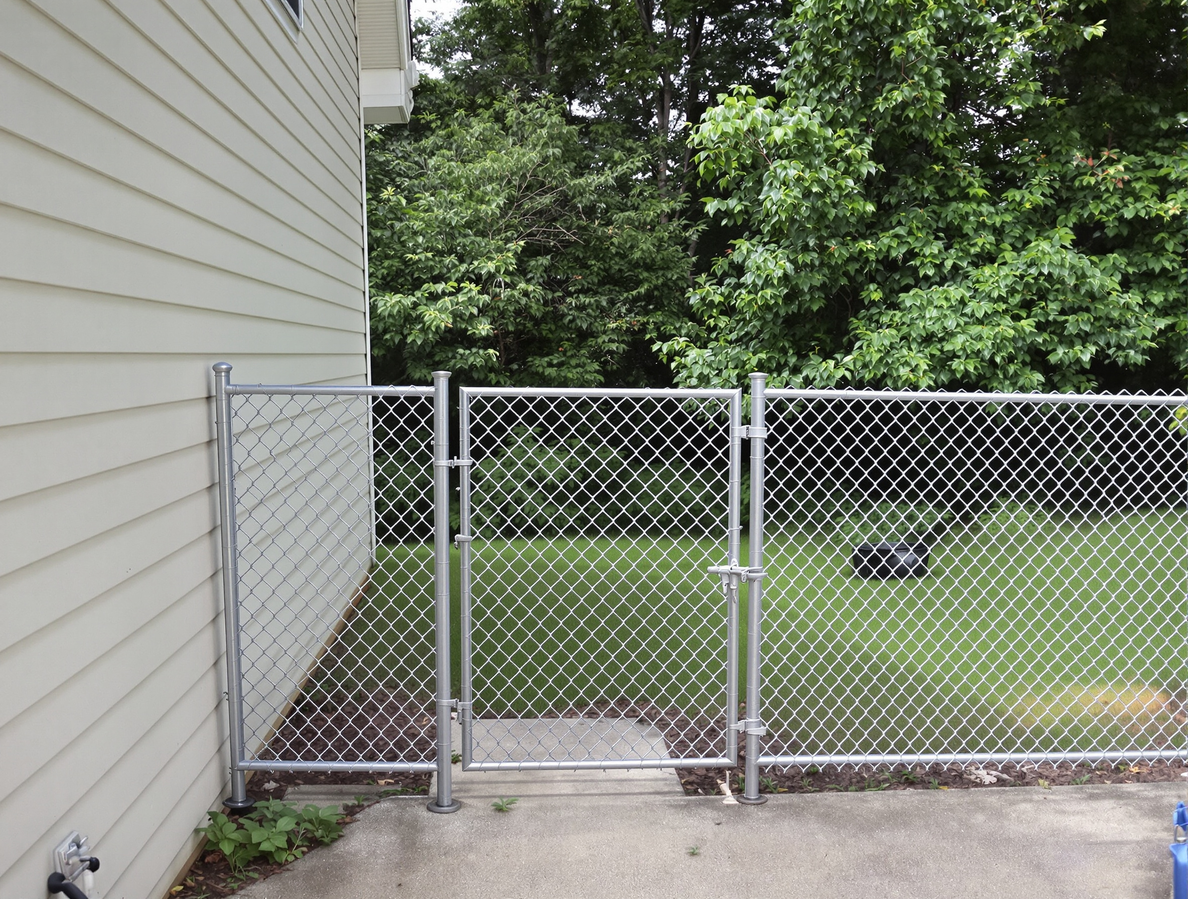 Residential backyard with silver chain-link fence and small swinging gate siding of 280875 - San Antonio Deck and Fence Works Metal chain-link fence beside house-deck builder-San Antonio, Texas