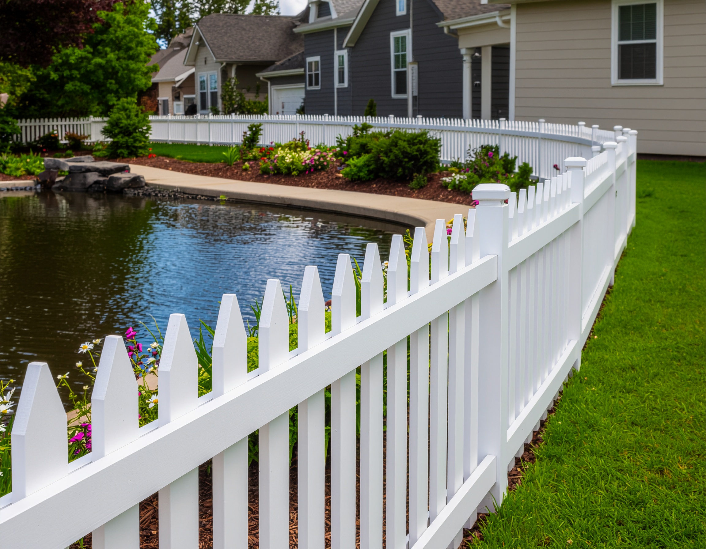 Suburban backyard bordered by a classic white picket fence with evenly spaced verti 333287 - San Antonio Deck and Fence Works White vinyl picket fence by pond.-deck builder-San Antonio, Texas